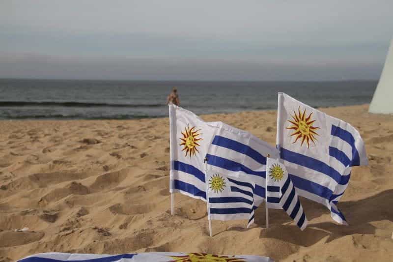 Four Uruguayan flags of different sizes in the sand at the beach.