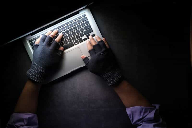 Hands in half gloves hover over a laptop keyboard.