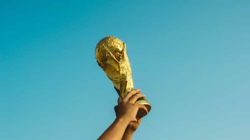 The FIFA World Cup trophy being held aloft against a blue sky.
