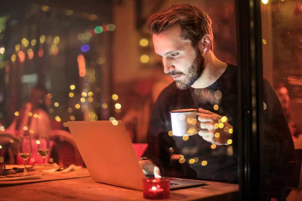 A man drinking a cup of coffee and using a laptop.