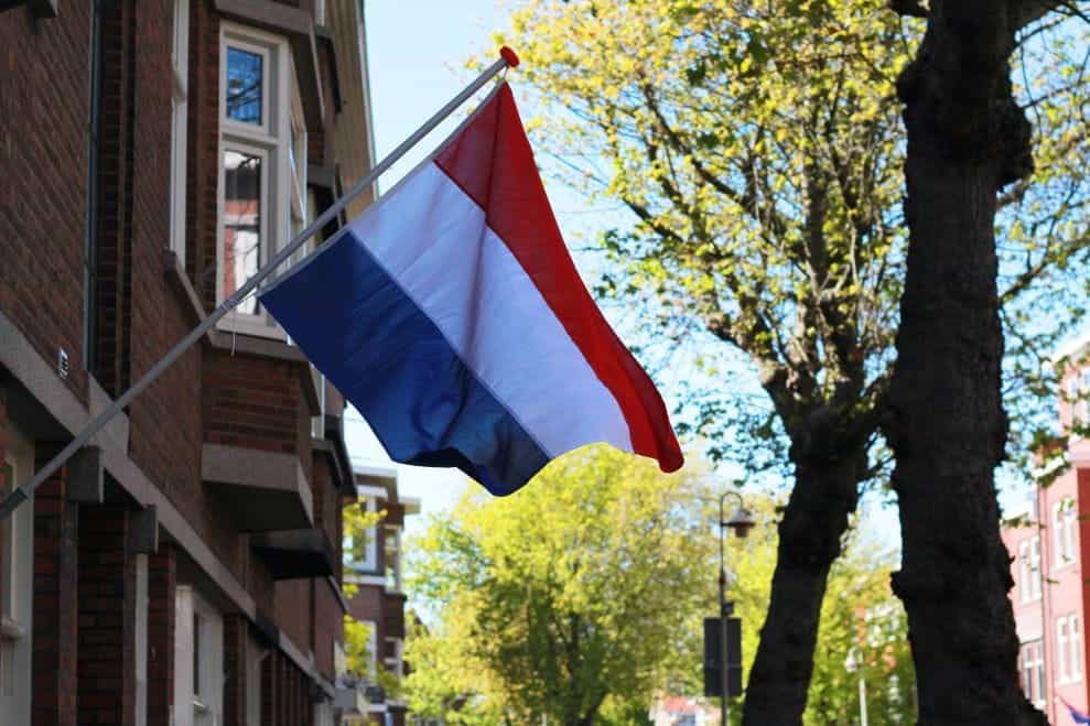 A Netherlands flag attached to an inclined pole at the front of a brick building.