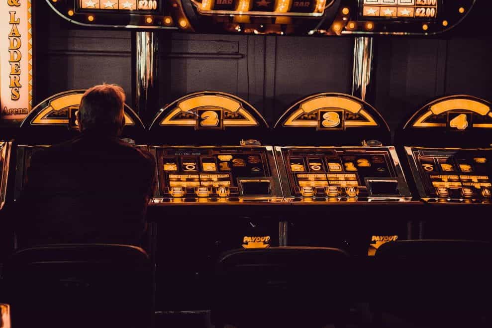 Someone sits in front of a bank of slot machines, lit in a yellowish light.