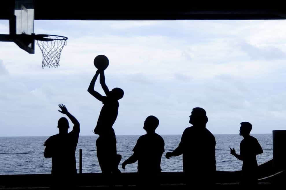 The black silhouettes of a group of people playing a game of basketball.