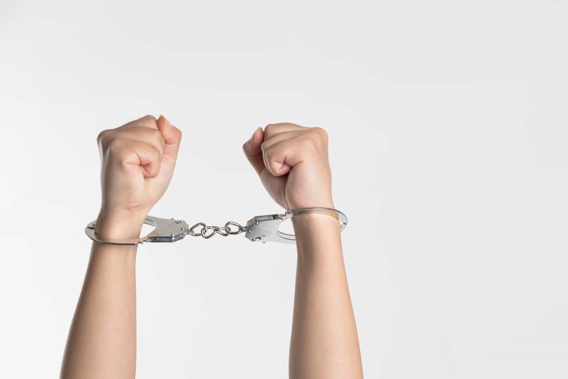 A person’s wrists are locked in handcuffs with their fists clenched.