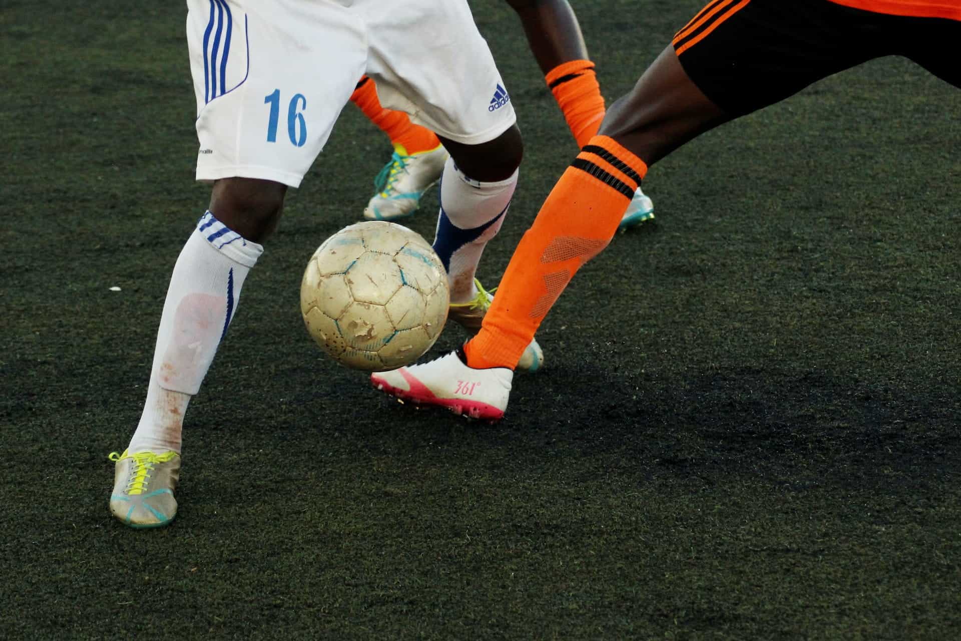 Multiple players’ legs reaching for a soccer ball during a match.