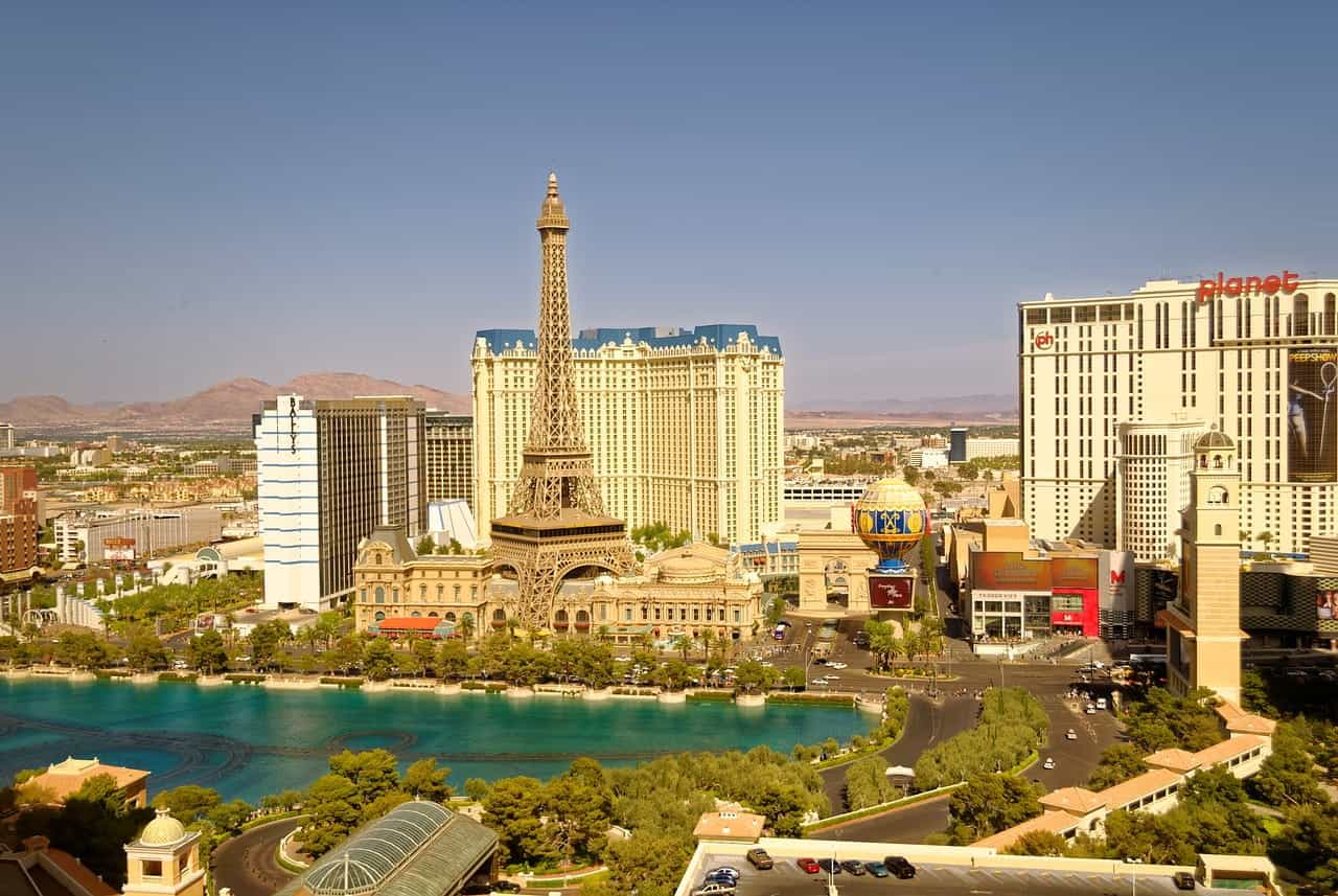 Several casinos and hotel resorts in downtown Las Vegas, Nevada, featuring a replica Eiffel Tower, a large fountain and pond, and mountains in the desert in the distance.