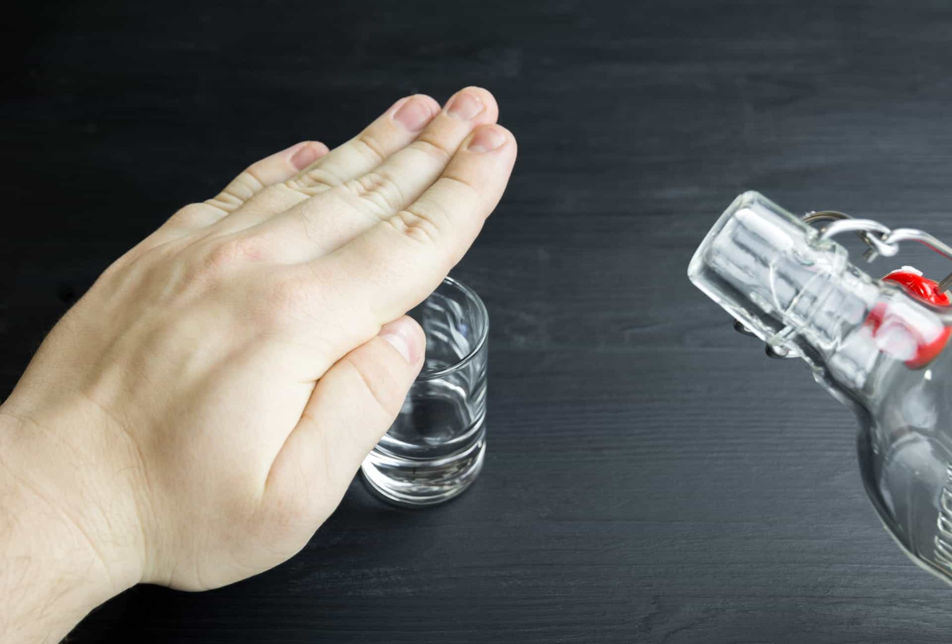 A hand is held over a shot glass, preventing more vodka being poured into it.