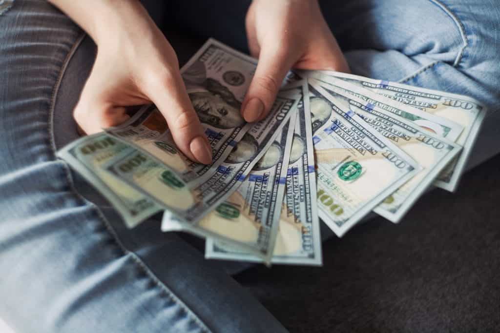 A pair of hands fans out many $100 USD bills.
