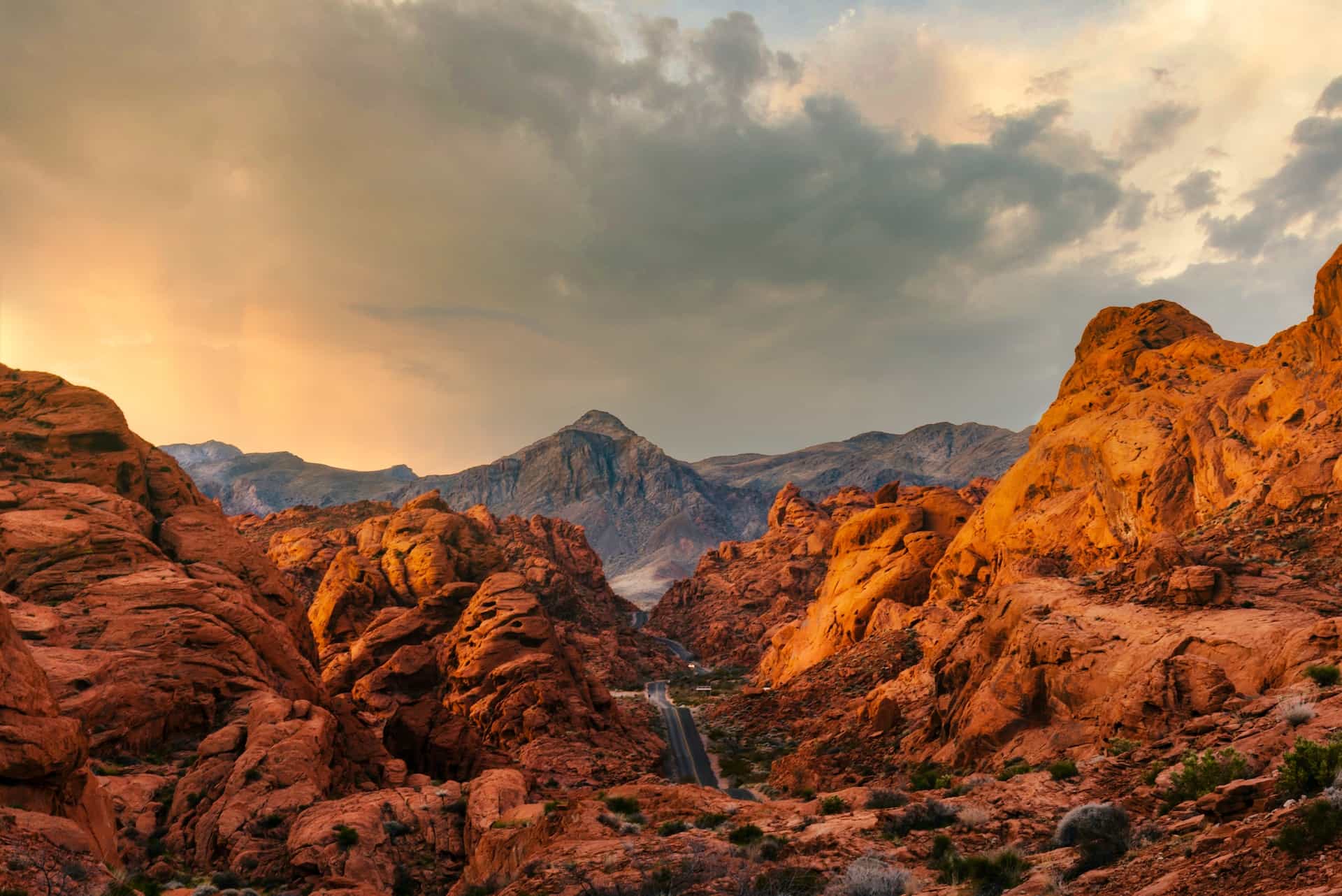 The hilly and scraggy Nevada desert, featuring a brick-red landscape with a road cutting through it, with tall mountains off in the distance.