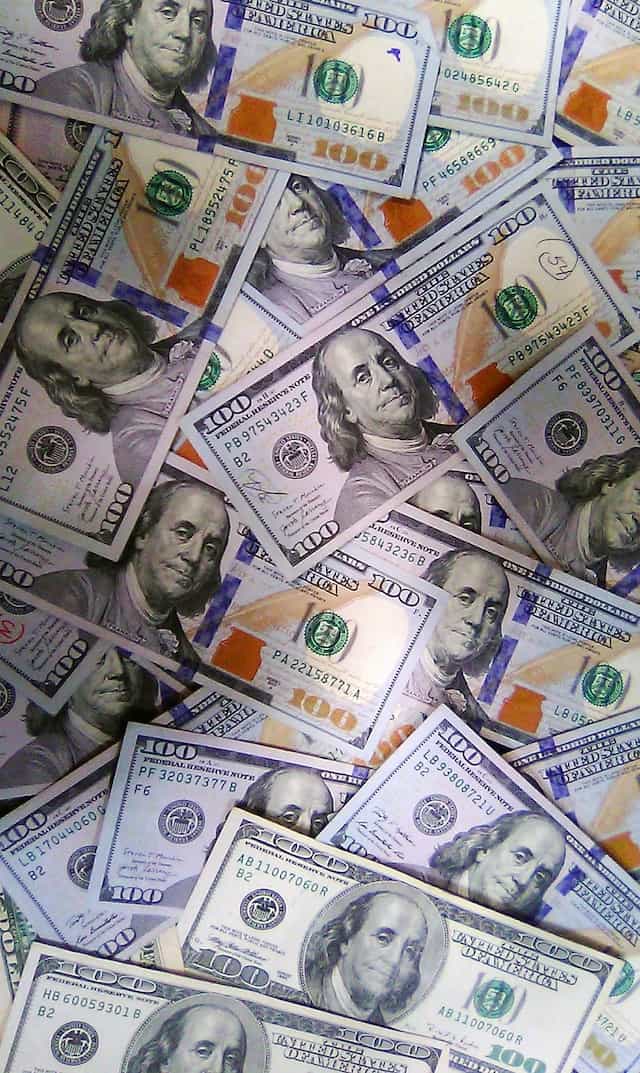 A scattering of several $100 US Dollar bills, featuring Benjamin Franklin’s face on them.