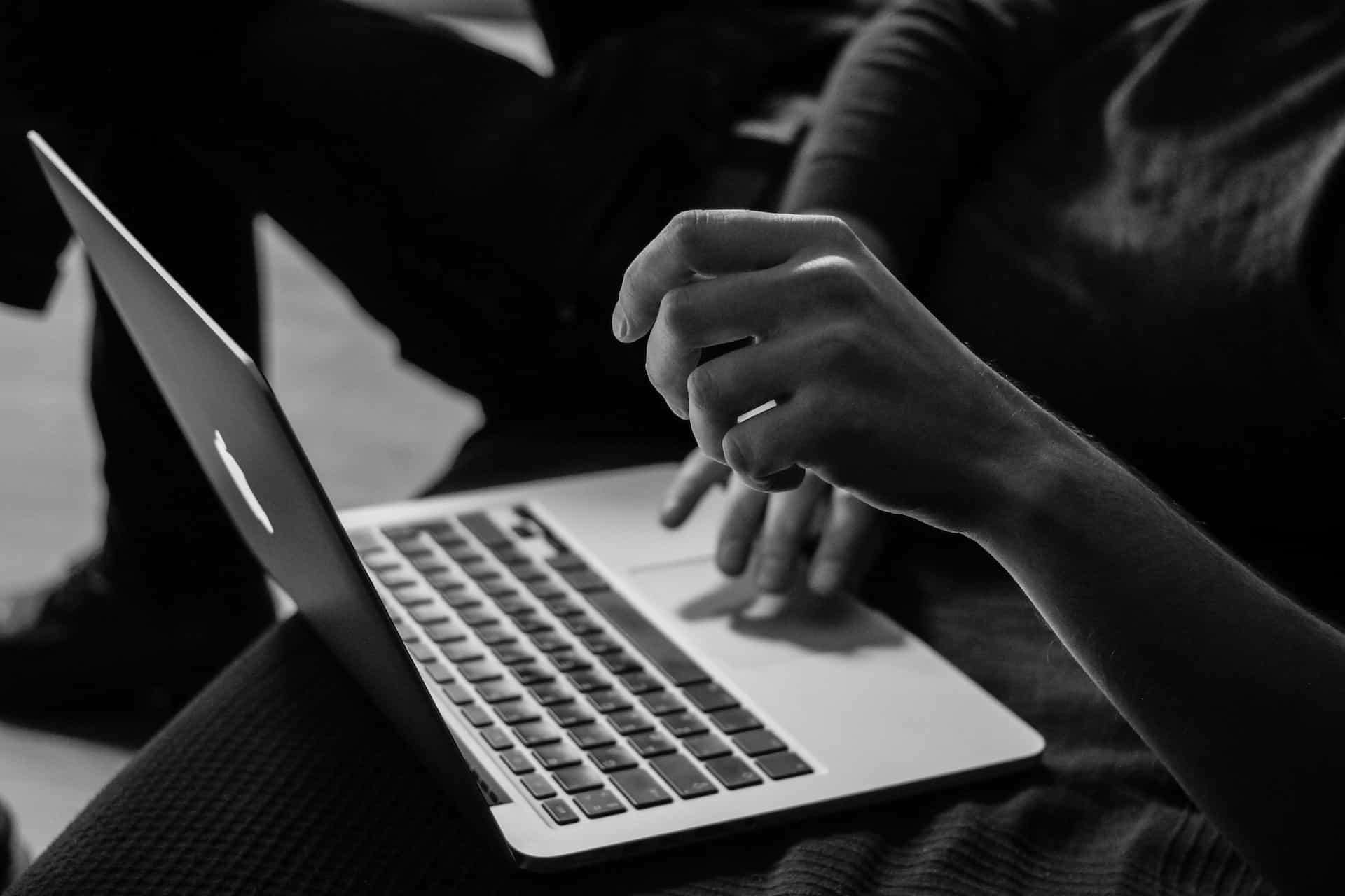 A person sitting down with a laptop, with one hand resting on the keyboard and another hovering slightly above the device.