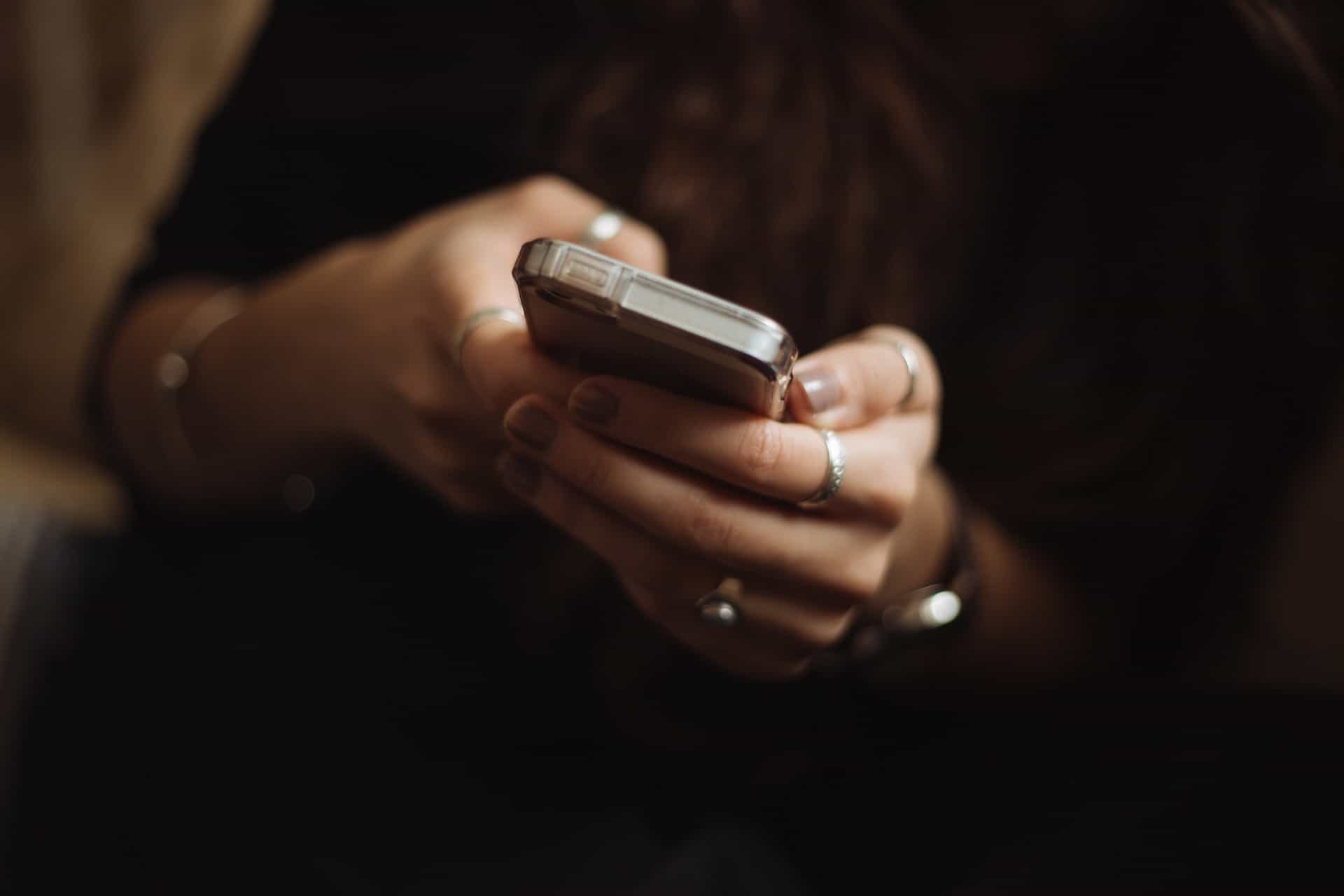 A person holding a small smartphone in both hands while using it.