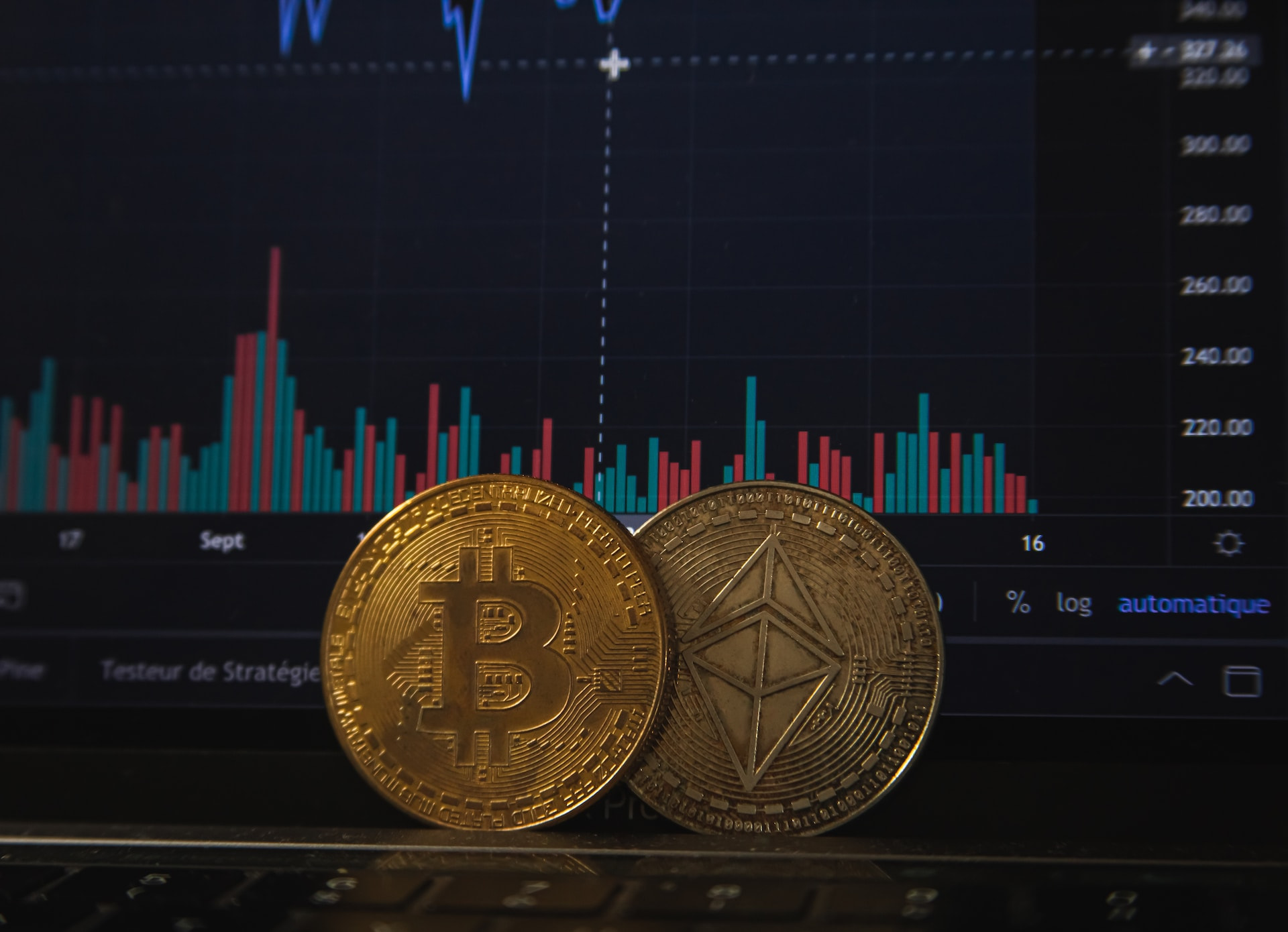 Two bitcoin coins sit in front of a computer screen depicting a chart.